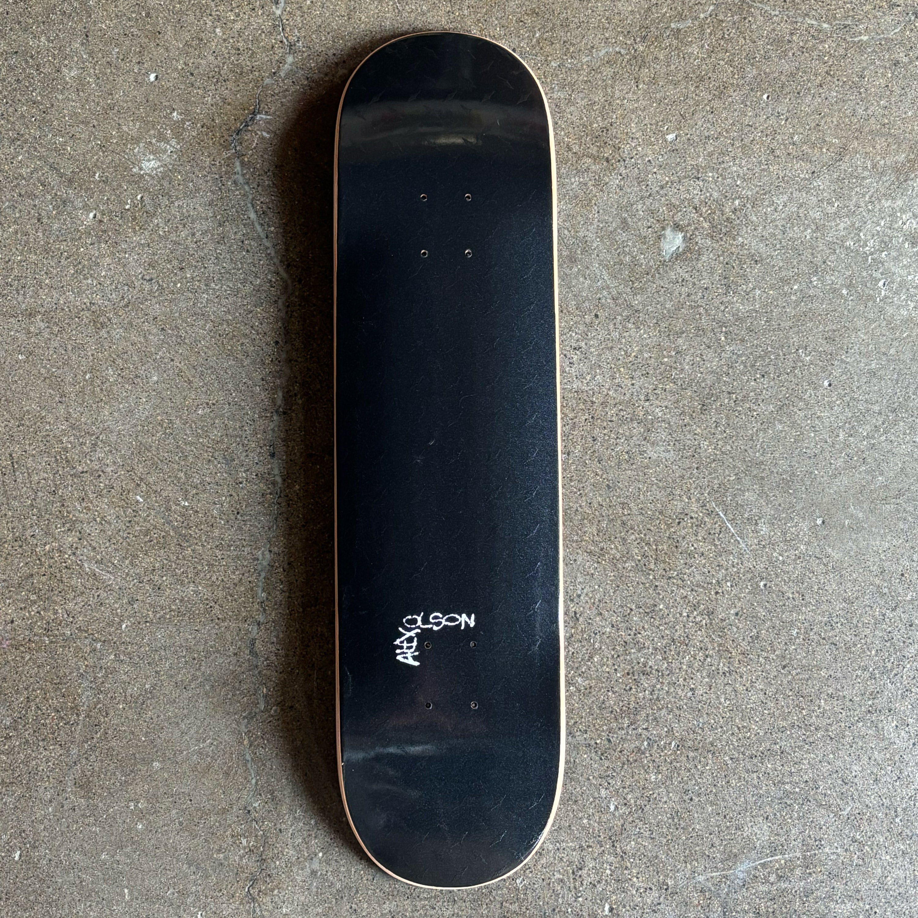 Full image of black deck with raised diamond plate and Alex Olson font on tail.